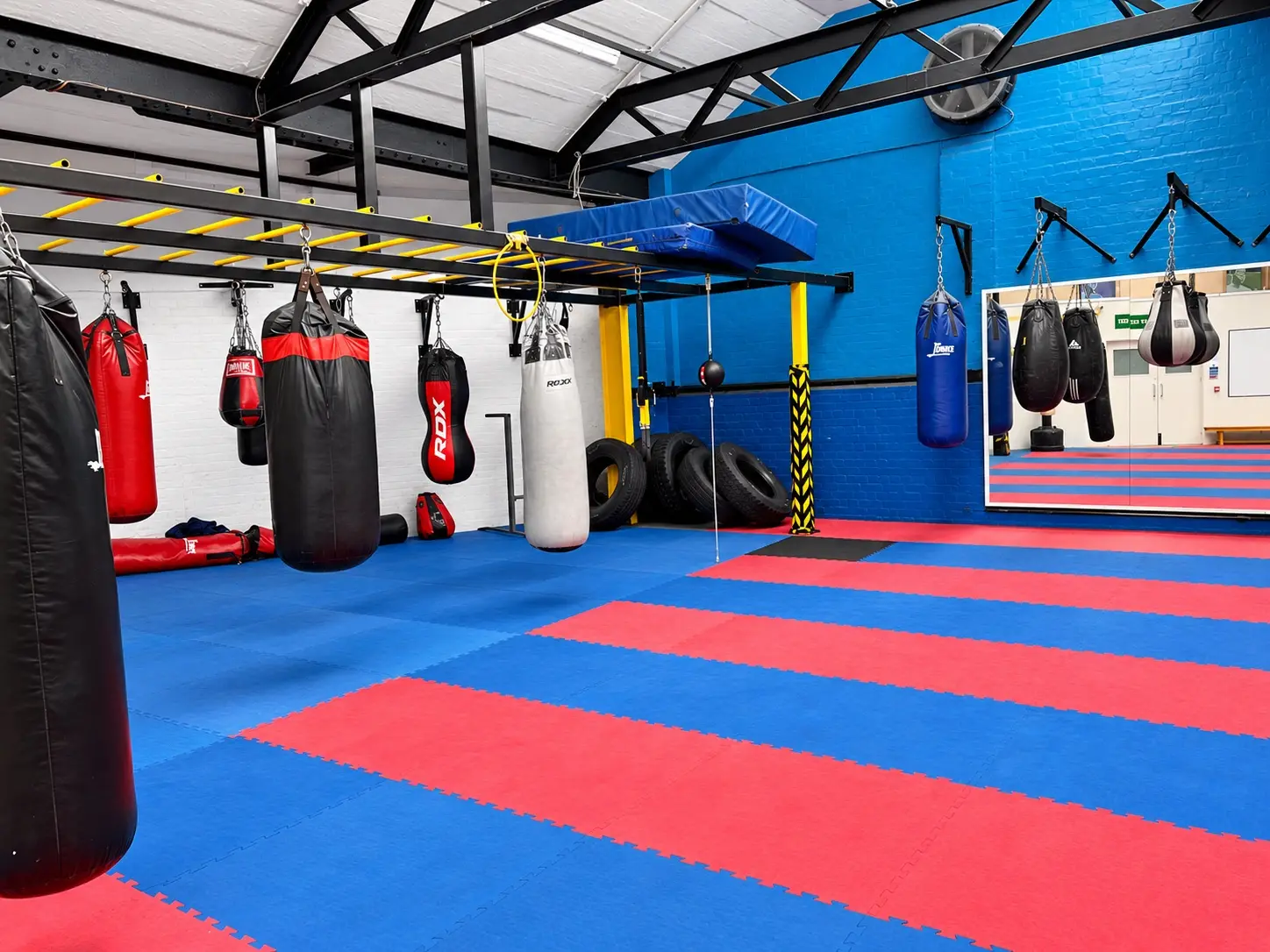 Punch bags hanging along the wall of the Waterfront gym, with tyres, monkey bars and red and blue matting