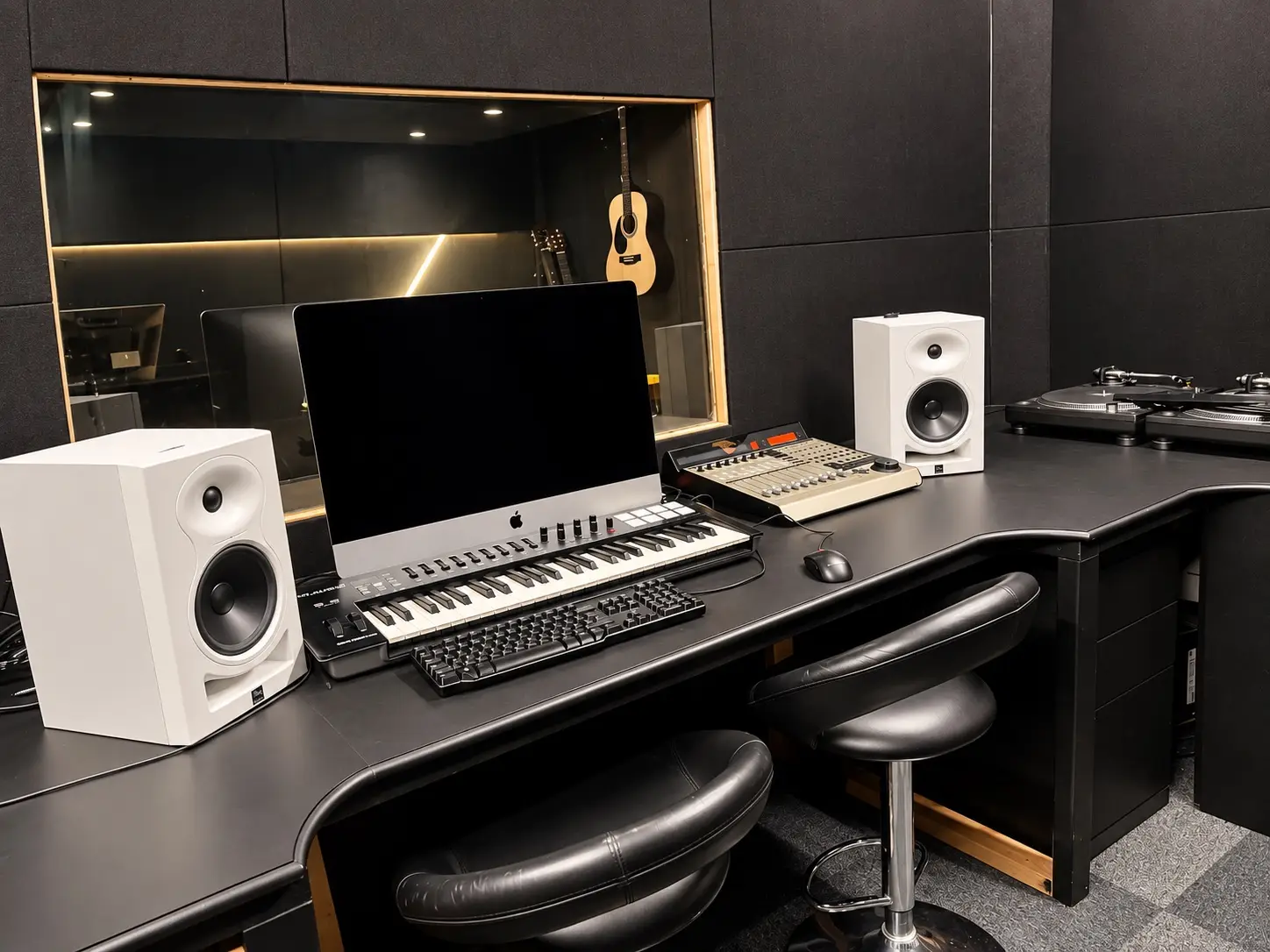 The Waterfront music studio, with a mixing desk, keyboard, monitor speakers and turntables, looking through to the live room